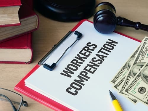 clipboard with paper that says 'workers' compensation' with pen and money on top