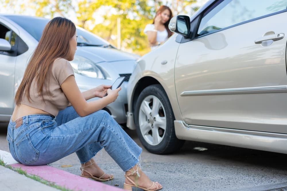 Two drivers inspect damage after a car accident, then take pictures and submit an online insurance claim. Idea: Online car accident insurance claims.